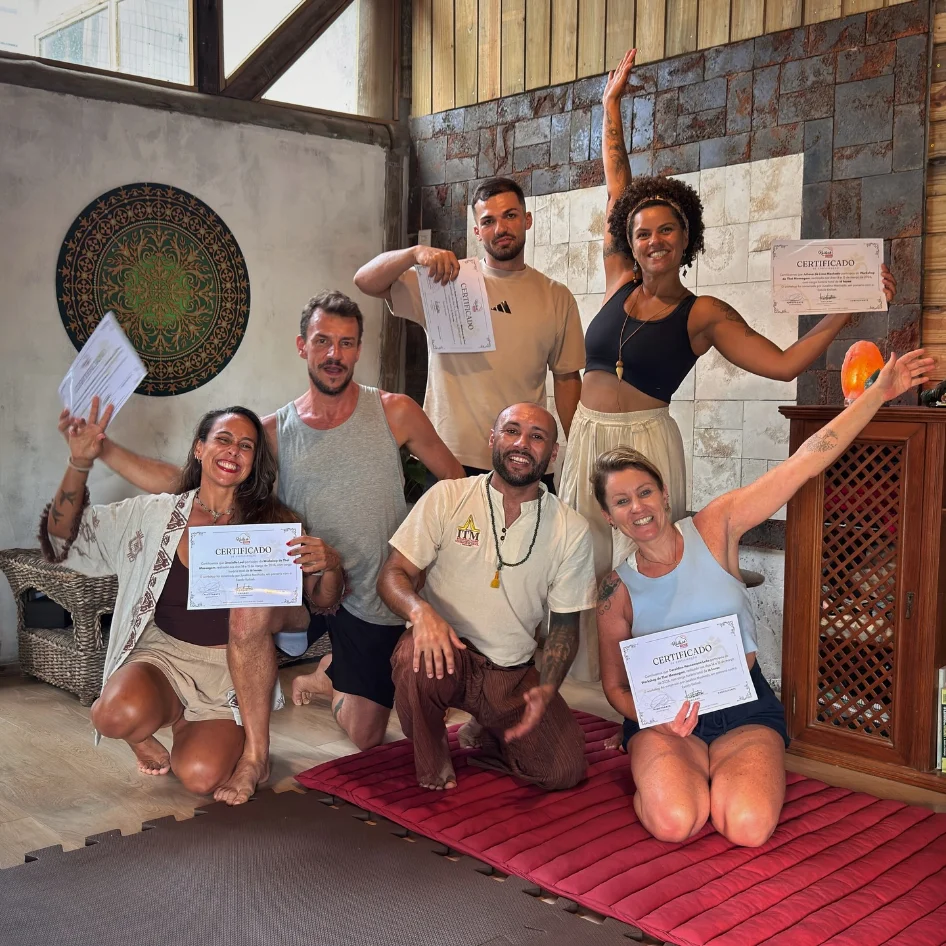 Turma de seis alunos comemorando com os certificados nas mãos, sobre o futon vermelho da sala de prática.